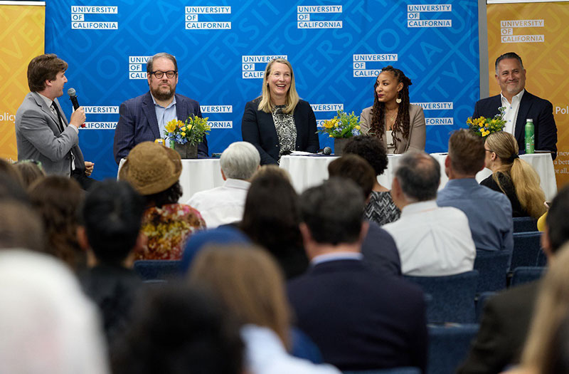 Panelists sitting in front of a University of California backdrop at an event.