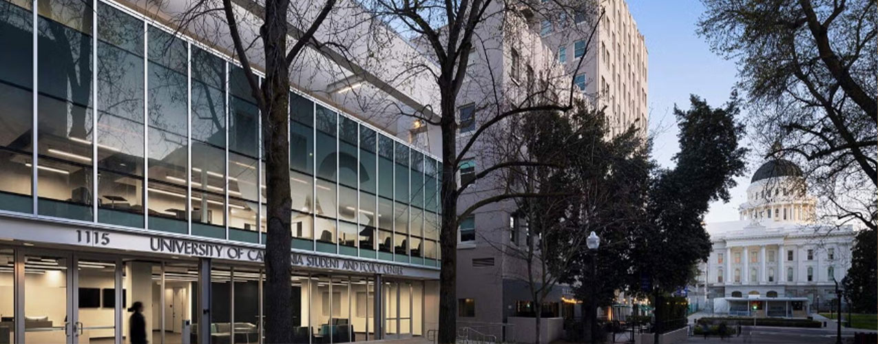 Entrance of the UC Student Policy Center Building with the dome of the California state capital building in the background.